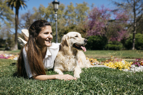 Glückliche Frau liegt mit ihrem Labrador Retriever auf einer Wiese im Stadtpark und genießt das Sonnenlicht - JRFF03154