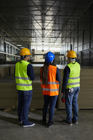 Rückansicht von Arbeitern, die am Gitter in einer Fabrik stehen, lizenzfreies Stockfoto