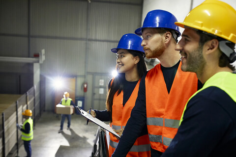Two men and smiling woman in reflective vests in factory stock photo