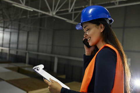 Lächelnde Arbeiterin am Telefon in einem Fabriklager, lizenzfreies Stockfoto