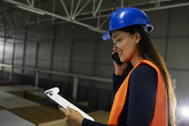 Smiling female worker on the phone in factory warehouse - ZEDF02241