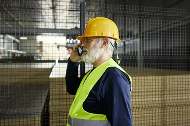 Älterer Arbeiter am Handy in einem Fabriklager - ZEDF02248