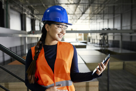 Lächelnde Arbeiterin mit Tablet in einem Fabriklager, lizenzfreies Stockfoto