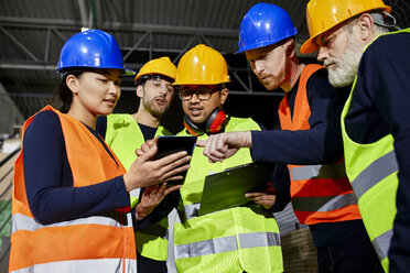 Arbeiter in einem Fabriklager, die sich unterhalten und ein Tablet benutzen - ZEDF02258