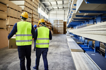 Rear view of two workers carrying boxes in factory warehouse - ZEDF02262