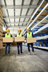 Three workers carrying boxes in factory warehouse - ZEDF02266