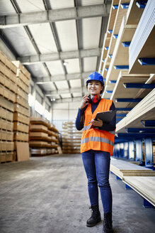 Porträt einer lächelnden Arbeiterin mit Zwischenablage in einem Fabriklager - ZEDF02268