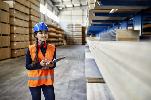 Lächelnde Arbeiterin mit Klemmbrett in einem Fabriklager - ZEDF02270