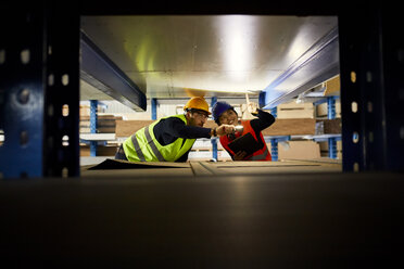 Zwei Arbeiter mit Taschenlampe suchen etwas in einem Fabriklager - ZEDF02281