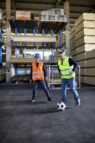 Arbeiter spielen Fußball in einem Fabriklager, lizenzfreies Stockfoto