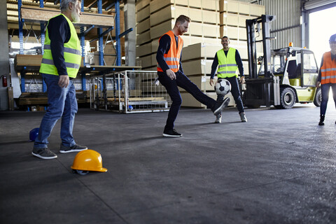 Arbeiter spielen Fußball in einem Fabriklager, lizenzfreies Stockfoto