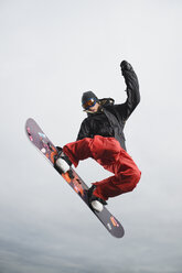 Gemischtrassiger Jugendlicher auf dem Snowboard in der Luft - BLEF00050