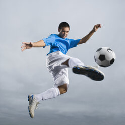 Gemischtrassiger Jugendlicher in der Luft, der einen Fußball kickt - BLEF00051