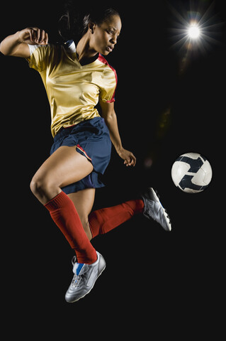Gemischtrassiger Fußballspieler, der den Ball in der Luft kickt, lizenzfreies Stockfoto