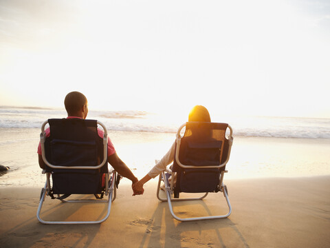 Paar hält Hände am Strand bei Sonnenuntergang, lizenzfreies Stockfoto