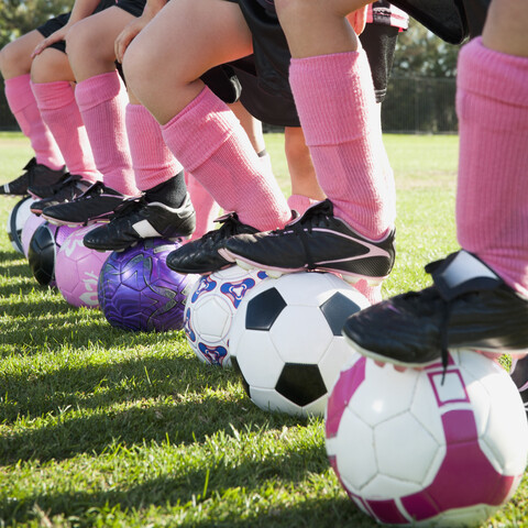 Fußballspielerinnen stehen mit den Füßen auf Fußbällen, lizenzfreies Stockfoto