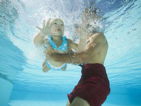 Gemischtrassiger Vater hält Tochter im Schwimmbad, lizenzfreies Stockfoto