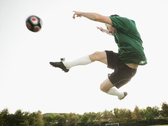 Kaukasischer Fußballspieler in der Luft, der einen Fußball tritt - BLEF00120