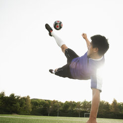 Asian soccer player in mid-air kicking soccer ball - BLEF00121