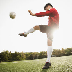 Asiatischer Fußballspieler, der den Ball auf dem Fußballfeld kickt - BLEF00122