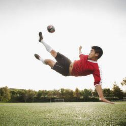 Asiatischer Fußballspieler in der Luft, der einen Fußball tritt - BLEF00123