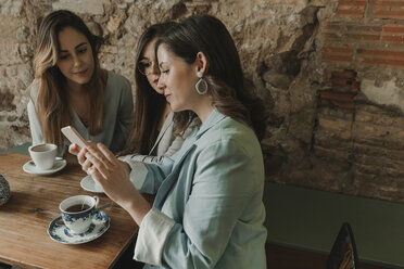 Drei junge Frauen mit einem Mobiltelefon in einem Cafe - AHSF00115