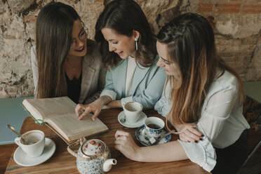 Drei junge Frauen lesen ein Buch in einem Café - AHSF00117