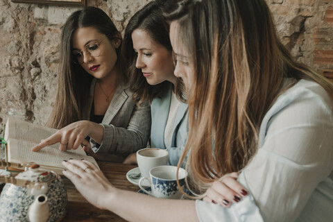 Drei junge Frauen lesen ein Buch in einem Café, lizenzfreies Stockfoto