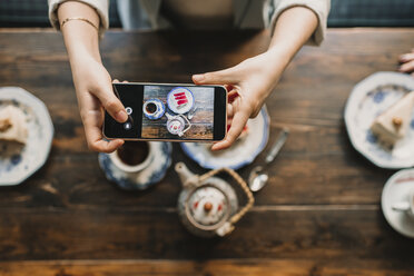 Top view of woman taking a photo of cake and tea in coffee shop - AHSF00131