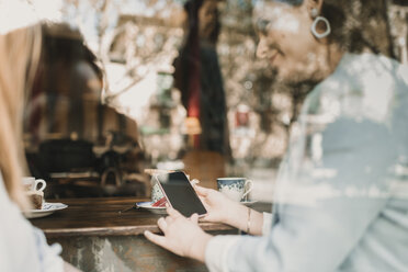 Junge Frau zeigt ihrer Freundin in einem Café ihr Handy - AHSF00134