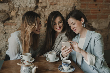 Drei junge Frauen schauen auf ein Handy in einem Café - AHSF00143