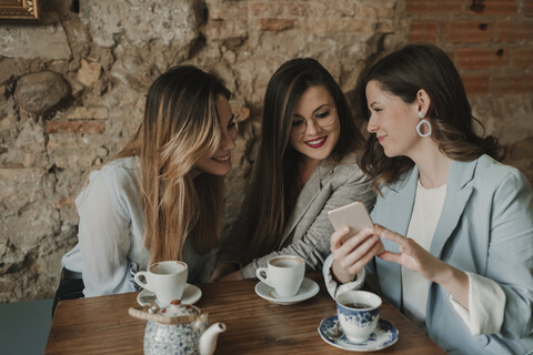 Drei junge Frauen schauen auf ein Handy in einem Café, lizenzfreies Stockfoto