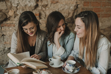 Drei glückliche junge Frauen lesen ein Buch in einem Café - AHSF00146