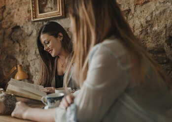 Zwei junge Frauen mit Buch in einem Cafe - AHSF00148