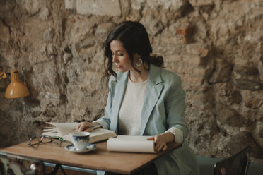 Junge Frau macht sich Notizen und liest ein Buch in einem Café - AHSF00155