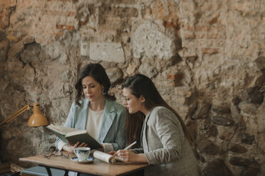 Zwei junge Frauen mit Notizbuch und Buch in einem Cafe - AHSF00156