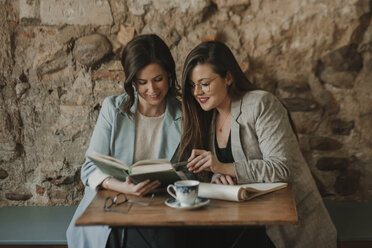 Zwei junge Frauen mit Notizbuch und Buch in einem Cafe - AHSF00157