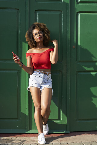 Frau in Rot mit ihrem Telefon an der grünen Tür, lizenzfreies Stockfoto