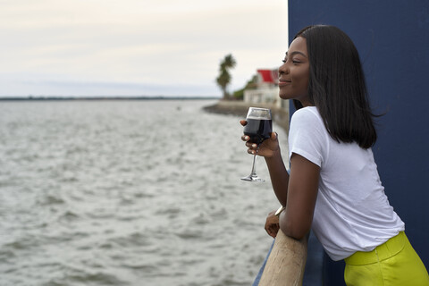 Glückliche junge Frau mit einem Glas Rotwein und Blick auf das Meer, lizenzfreies Stockfoto