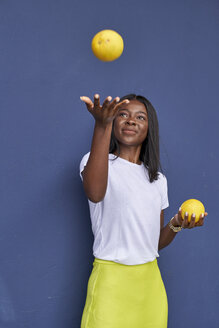 Porträt einer glücklichen jungen Frau, die mit zwei Orangen vor einem blauen Hintergrund jongliert - VEGF00079