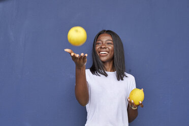 Portrait of happy young woman juggling with two oranges in front of blue background - VEGF00080