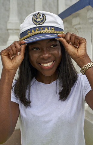 Porträt einer glücklichen jungen Frau mit Kapitänsmütze, lizenzfreies Stockfoto