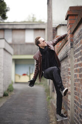 Young man climbing over brick wall - EYAF00172