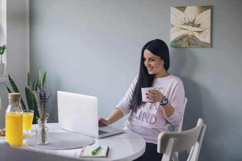 Schöne junge Frau, die im Internet surft und zu Hause Kaffee trinkt - MOMF00698