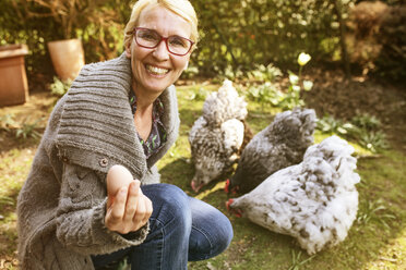 Porträt einer glücklichen Frau im Garten mit ihren Orpington-Hennen, die ein Ei zeigen - JATF01137
