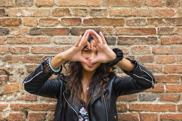 Portrait of young making heart shape with hands and fingers, brick wall - MGIF00395
