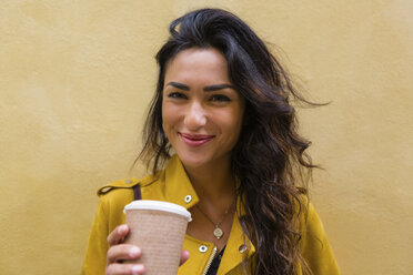 Porträt einer jungen Frau in gelber Lederjacke, die eine Tasse Kaffee in der Hand hält - MGIF00409