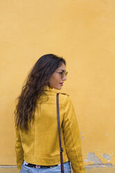 Portrait of young woman wearing yellow leather jacket and sun glasses, rear view - MGIF00413