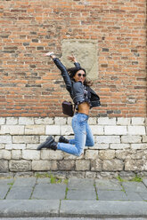 Junge Frau springt in die Luft, im Hintergrund eine Ziegelmauer - MGIF00414