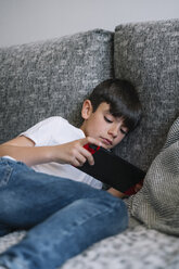 Boy lying on the couch playing computer game - JCMF00040